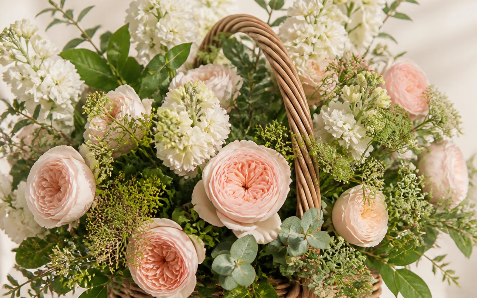 Low woven flower basket with blush, ivory, and fresh-green flowers