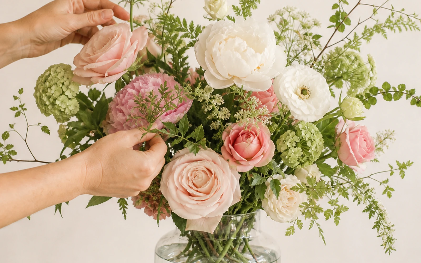 Florist making the final correction to a balanced blush and ivory vase arrangement