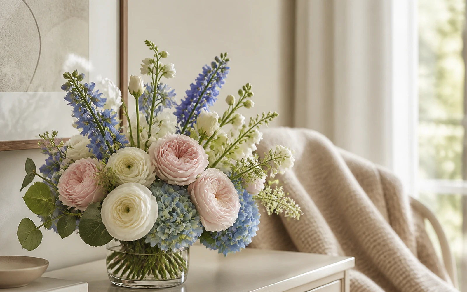 A compact blue, blush, ivory, and green arrangement on a stable console in a calm home.