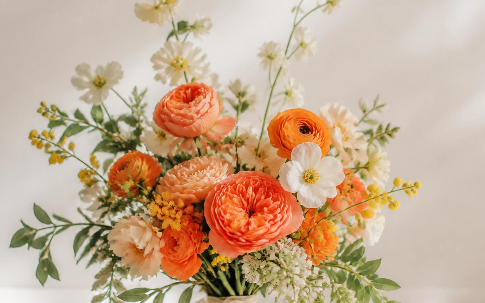 Warm airy wedding bouquet in coral, peach, yellow, ivory, and green