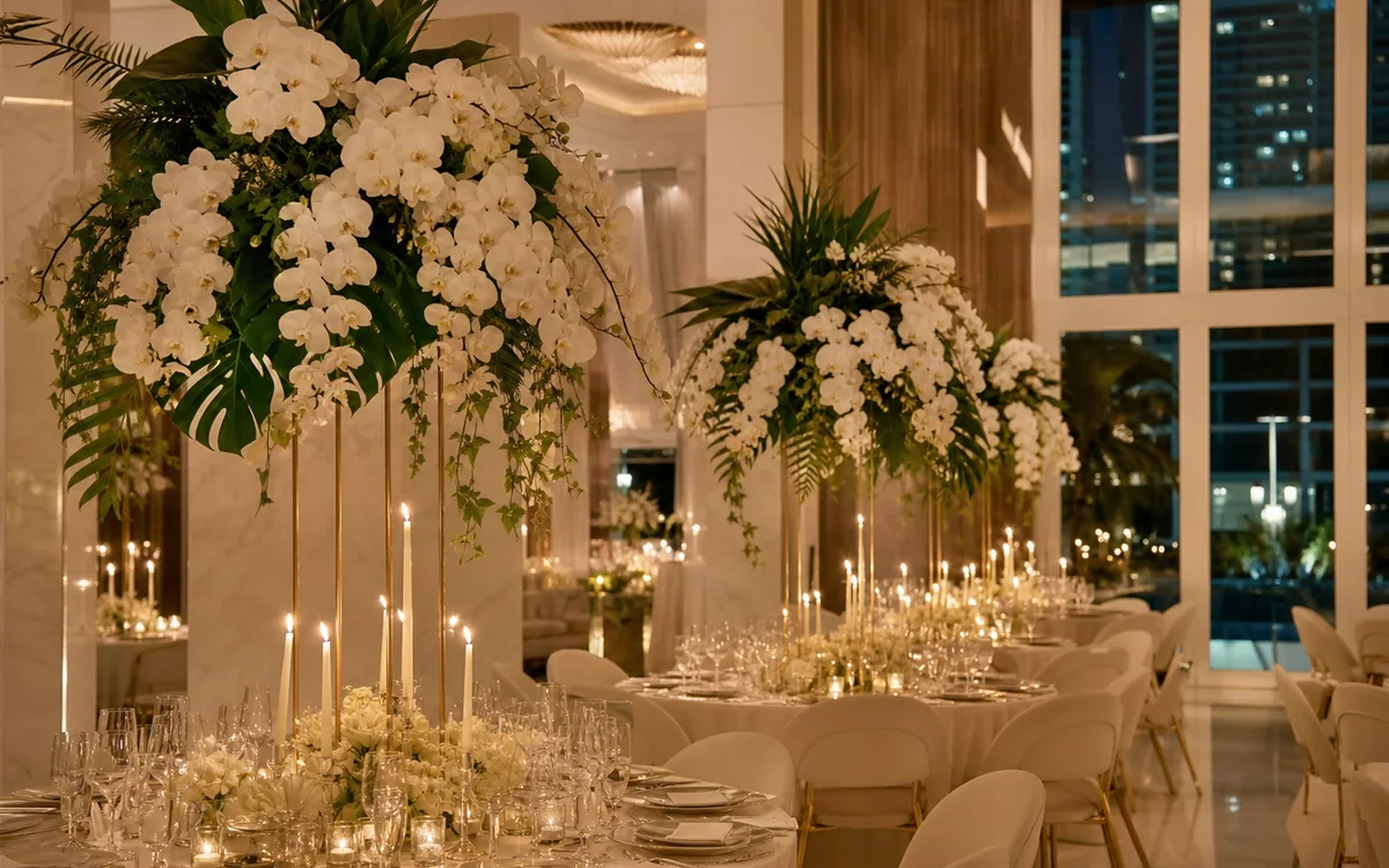 Tall white floral installations and candlelit dinner tables in an elegant event room.